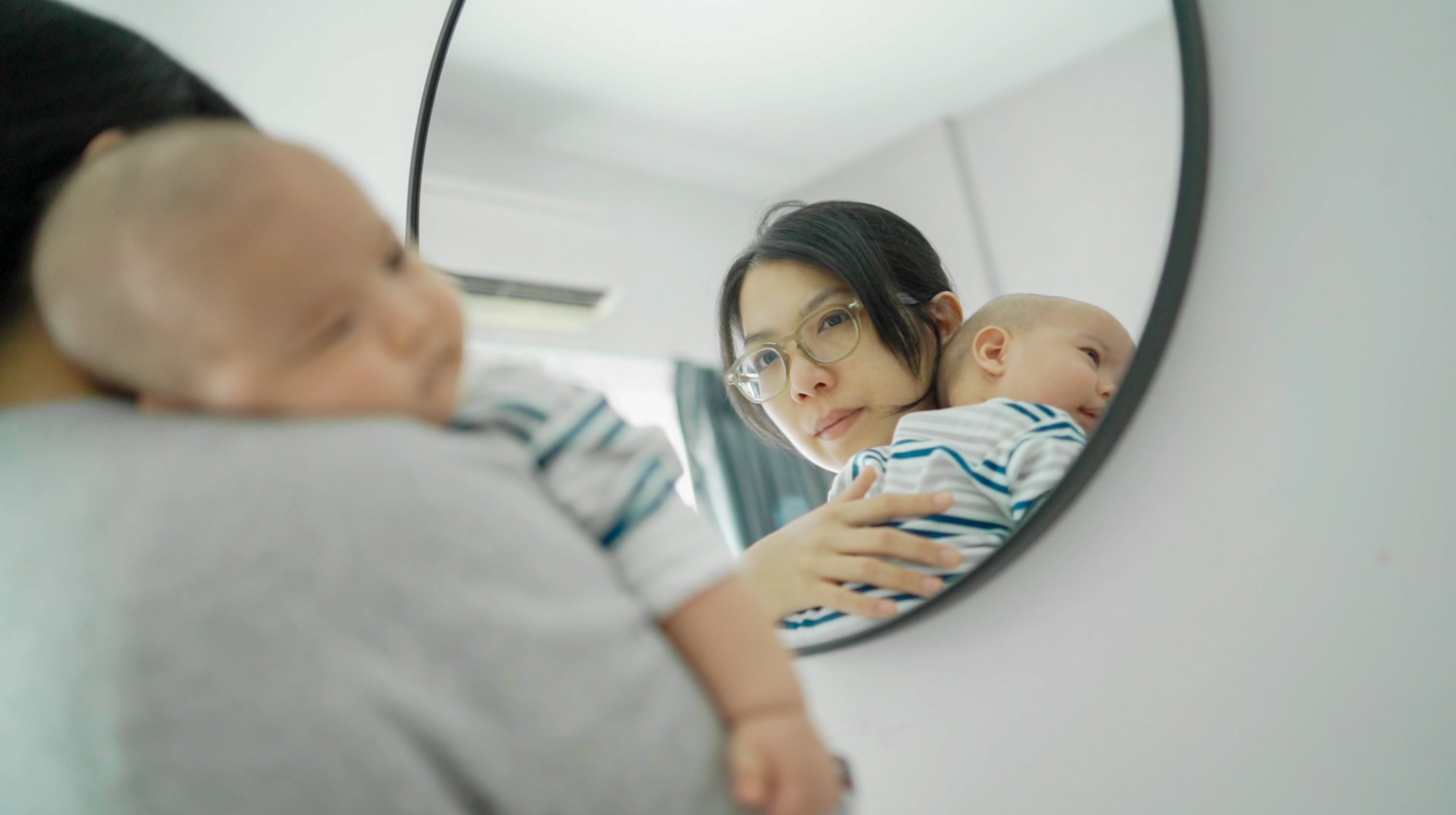 A woman holding a baby and looking into a mirror