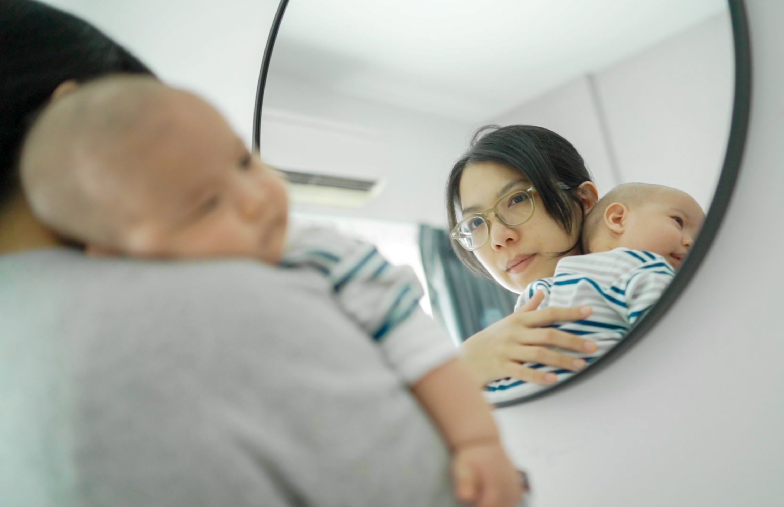 A woman holding a baby and looking into a mirror